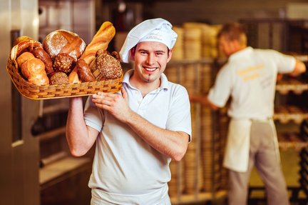 Bäcker mit Brotkorb in der Backstube Ein junger Baecker in weisser Kleidung traegt einen Korb mit Broten und Broetchen auf der Schulter
