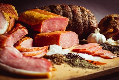 Geräucherte Fleischerzeugnisse auf dem Holzbrett Angeschnittener Kassler, Schinken und ein in Pfeffer gewaelzter Braten liegen auf einem Holzbrett, daneben Knoblauch und Gewuerze